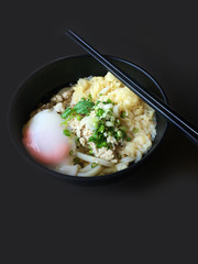 Bowl of japanese food, noodles with egg onsen in black bowl background.