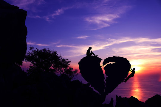 Women sitting and Men climbing on broken heart-shaped stone on a mountain with purple sky sunset background.Silhouette Valentine background concept.