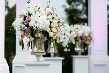 Silver vases with large white bouquets stand on pillars outside