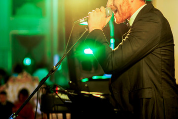 Green light illuminates bearded man in black suit singing on the