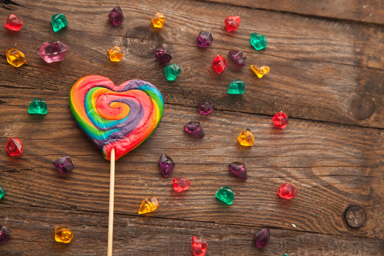 Sweet colorful lollipop in the shape of a heart on wooden background. Concept for Valentine's day.