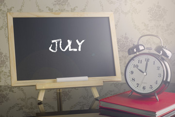 July on chalkboard with alarm clock.