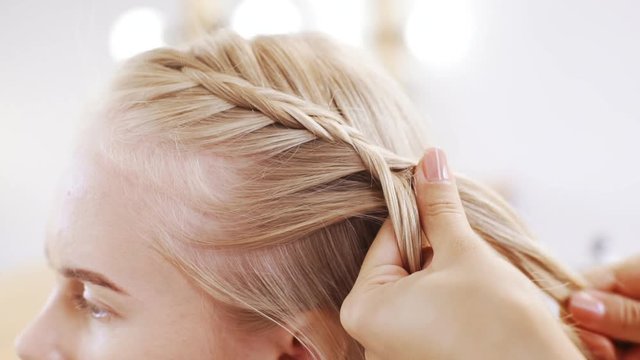 Hairdresser plaiting braids to blonde girl in beauty salon Slow motion Close up