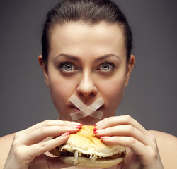 Diet concept: woman holding a burger with mouth sealed