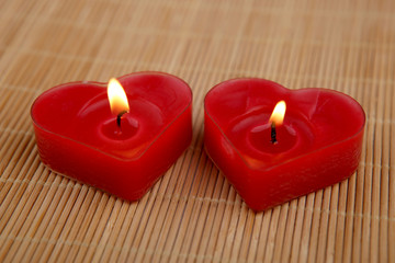 Obraz na płótnie Canvas Heart shape candles. Two red candles burning on bamboo mat. 