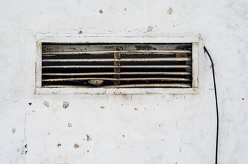 Rusty old ventilation grille in the wall with a wire