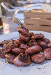 Piece of sausage caught with fork. Grilled sausages from Aragon Teruel Spain, Cut into pieces, typical tapas dish. Close-up. Blurred background basket of bread and soda