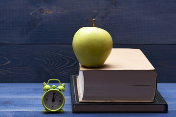 Books, green apple and alarm clock