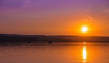 wonderful warm sunrise over the lake. people in the boats fishing. majestic landscape. used as background