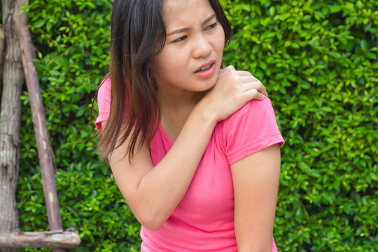 Young woman shoulder or joint pain in garden, injury concept.