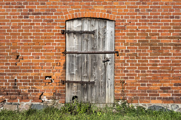 Old wooden door with metal fittings, red brick stone facade and green lawn.