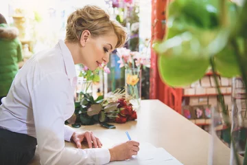 Store enrouleur tamisant Fleuriste Cheerful woman making notes in flower shop
