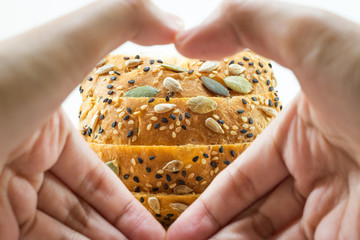 Fresh sliced bread with sunflower and sesame seeds; Heart hands for healthy background.