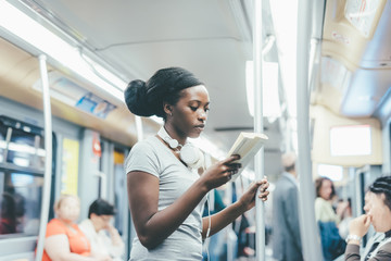 Young beautiful black woman sitting on subway reading a book - commuter, student, knowledge concept