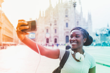 Young black woman taking selfie with smart phone hand hold with Milan cathedral in background,...