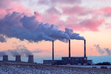 Thermal power plant in the cold winter landscape. Pipe with smoke against the pink sunset sky