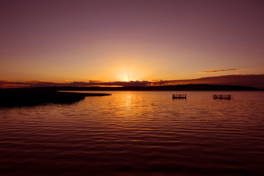 Germany, Kummerow: Atmospheric colorful sunset with lake, sunbeams, weirs, reed, horizon and sky.