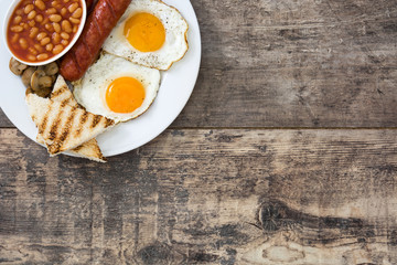 Traditional full English breakfast with fried eggs, sausages, beans, mushrooms, grilled tomatoes and bacon on wooden background

