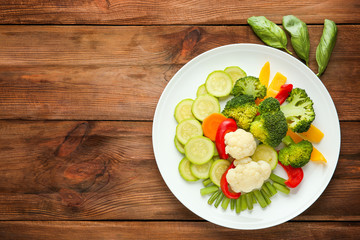Plate with fresh vegetables on wooden background