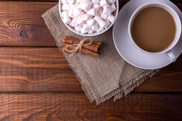 Cup of cocoa and plate with marshmallows and cinnamon on wooden background
