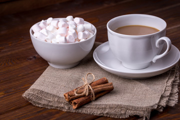 Cup of cocoa and plate with marshmallows and cinnamon on wooden background