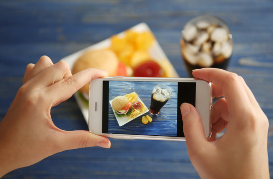 Female hands taking photo of tasty burger with snacks on table