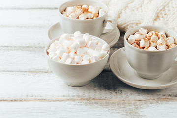 Cups with hot coffee or cocoa and marshmallows, white knitted blanked 