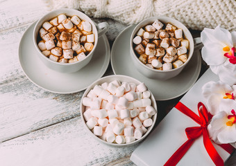 Cups with hot coffee or cocoa and marshmallows, gift box with red ribbon
