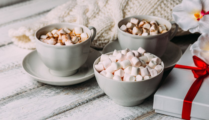 Cups with hot coffee or cocoa and marshmallows, gift box with red ribbon