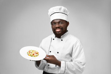 African American chef with plate of tasty salad on light background
