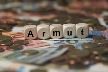 armut - Holzwürfel mit Buchstaben im Hintergrund mit Geld, Geldscheine