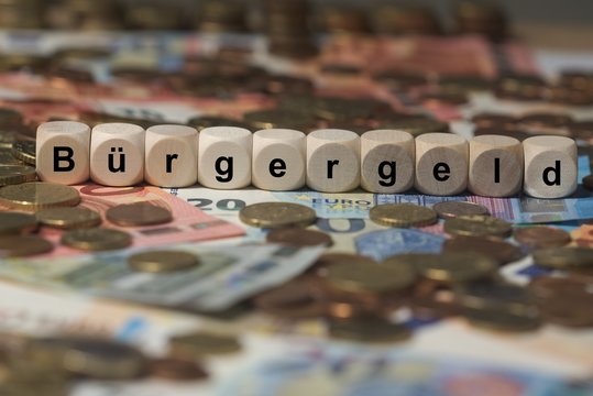 bürgergeld - Holzwürfel mit Buchstaben im Hintergrund mit Geld, Geldscheine