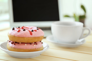Delicious donuts with cup of tea and laptop on wooden table  closeup
