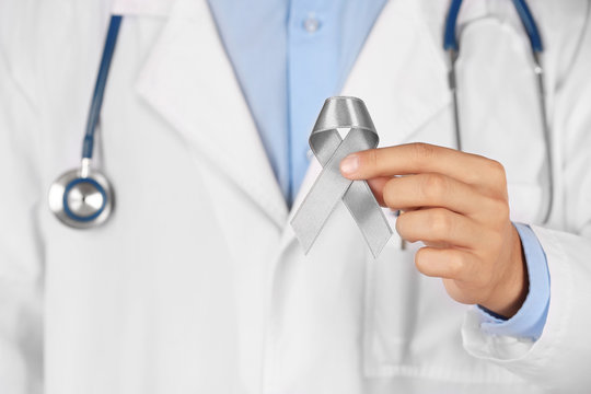 Doctor holding grey ribbon, close up view. Brain cancer, diabetes, asthma concept