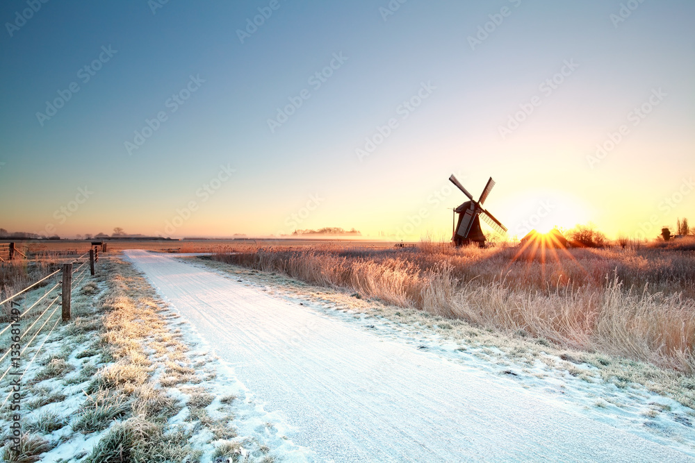 Wall mural snow on bike path and sun behind windmill