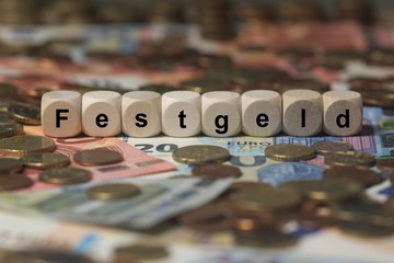 festgeld - Holzwürfel mit Buchstaben im Hintergrund mit Geld, Geldscheine