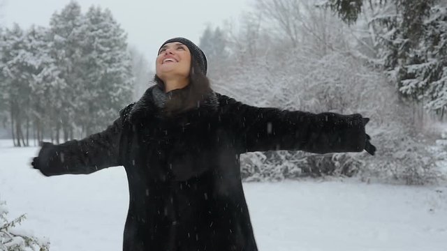Beautiful woman is dancing in a winter park. It is snowing. She is happy in winter. She is smiling. Slow motion.