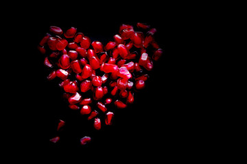 Heart from red juicy grains of pomegranate on a black surface. Gift by St. Valentine's Day.
