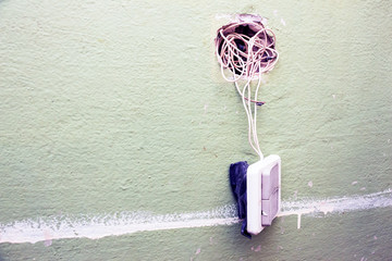 A broken light switch with exposed wires on a dirty old wall