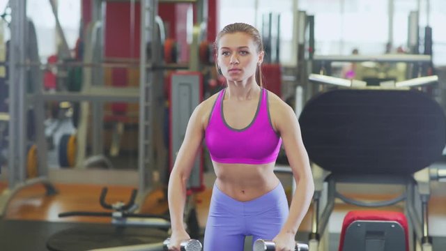 Sports young woman with a good figure in the gym. Young woman with a beautiful trained body doing exercise with dumbbells. Woman involved in sports and enjoys training. Beautiful body relief