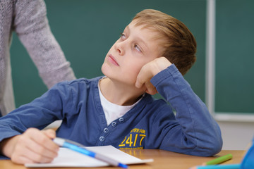 junge in der grundschule stützt genervt den kopf auf und schaut die lehrerin an