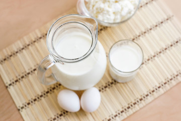 Fresh milk in glass jug and glass, eggs, cottage cheese on wood table background, country rustic still life. Dairy products. Vintage Tone. Top view.