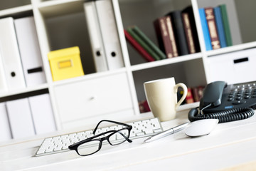 Office workplace with computer, keyboard, coffee and bookshelf