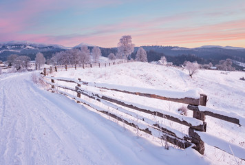 Winter country landscape with timber fence and snowy road into evergreen forest