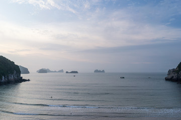 Scenic view of ocean shore with fisherman on wooden boat before sunrise.