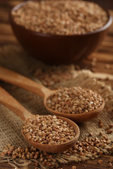 Buckwheat seeds in wooden spoon on a brown wooden table