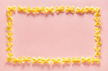 Frame from wheat pasta farfalle on rose background. Random pattern. Flat lay