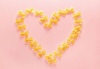 Heart frame from wheat pasta farfalle on rose background. Valentine's day.