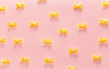 Ornament from wheat pasta farfalle on rose background. Random pattern. Flat lay