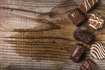 Different types of chocolate candy on wood background with copy